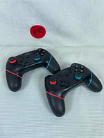 Photo showing two black wireless gaming controllers with red and blue accents laid on a white surface.