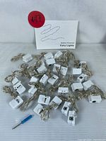 Image showing approximately 30 individual sets of battery powered fairy lights neatly laid out, each with small white battery packs and long thin wires.