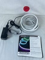 Coiled white neon LED light strip with attached power adapter, control module, and user manual placed on white surface.
