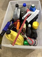 Photo showing multiple automotive chemical bottles in a plastic bin with two cleaning brushes on top.