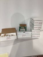 Multiple boxes of Christmas ornaments, stacked and displayed on white surface.