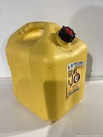 Side view of yellow plastic fuel can showing handle and black/red cap.