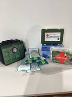Photo showing multiple first aid supplies including green and clear Johnson & Johnson kits and boxed nitrile gloves.