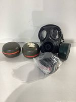 Photo showing black NATO German gas mask with two olive green round filters and one sealed filter cartridge