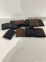 Ten men's wallets arranged on white surface, showing various colors and styles, mostly black and brown leather wallets with one featuring a Harley Davidson emblem and one branded Levi's.
