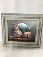 Framed still life painting showing Native American pottery and floral elements with signature visible.