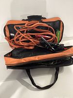 Orange jumper cables coiled inside a black and orange zippered storage bag with handles.