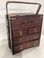 Front view of Korean style wood storage chest showing carved drawer fronts, metal corner accents, four drawers with metal pull tabs, one pull tab missing, and a top handle.