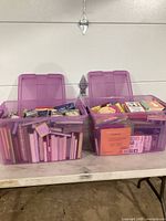 Two large purple plastic storage totes filled with children's books, lids open, showing a mix of book sizes and colorful covers.