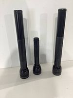 Three black MagLite flashlights of different lengths standing upright.