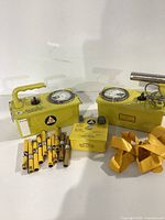 Lot view showing two yellow Victoreen radiation detectors, yellow cylindrical test sources, an accessory box, and a yellow strap
