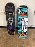 Two skateboards standing vertically side by side against a wall, showing overall graphics and wheels.