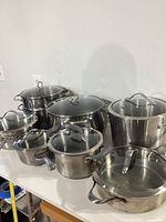 Six stainless steel cookware pieces with lids arranged on countertop
