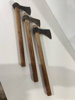 Photo showing the full length of three throwing axes laid out on a white surface, wooden handles and metal axe heads visible.