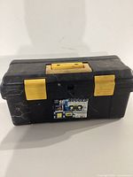 Closed black plastic toolbox with yellow handle and latches, label showing '16 Rugged'