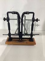 Front view of the Warthog knife sharpener showing the adjustment screws and sharpening stones on black metal frames, mounted on a wooden base.