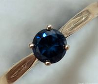 Close-up view of round blue diamond on yellow gold band showing the prongs and diamond facets.