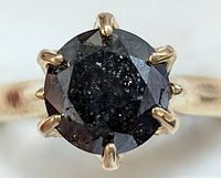 Top-down close-up of round black diamond in six-prong yellow gold setting