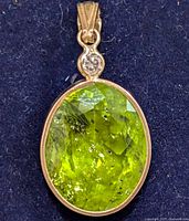 Clear top-down view of the oval green peridot and diamond pendant on a dark fabric background.