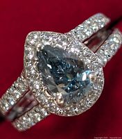 Close-up of pear-shaped blue lab-created diamond with surrounding cubic zirconia stones on sterling silver ring.