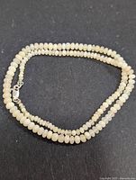 Single strand freshwater pearl necklace laid out on black background, showing clasp and pearl sizes.