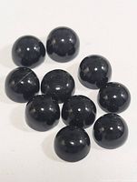 Ten polished black onyx cabochon gemstones displayed on a white surface. Each stone is round and domed with a smooth reflective surface.