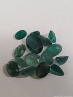 Close up of multiple genuine emerald gemstones with varying shapes and sizes, placed on white background to show color and cut details.