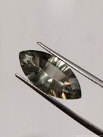 Close-up of the marquise cut green amethyst held by tweezers with reflective facets visible.