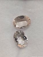 Two oval faceted morganite gemstones viewed from top showing clarity and color differences. One appears peach-pink, the other lighter near colorless.