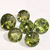 Six round cut peridot gemstones arranged on a white background showing color and inclusions.