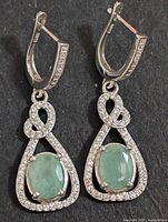 Close-up front view of the silver drop earrings showing oval emerald stones surrounded by cubic zirconia stones on black background.