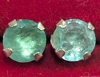 Close-up image of two round emerald stones set in silver prongs, showing stone clarity and prong details.