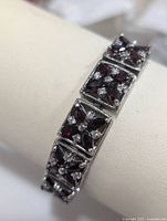 Close-up of bracelet showing square silver links with dark red garnet stones and small clear cubic zirconia stones set in floral pattern.