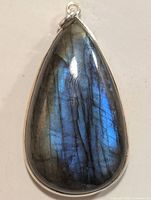 Front view of teardrop-shaped labradorite pendant displaying blue and green iridescence within silver setting, showing natural veining and polish.