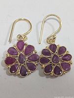 Pair of silver hook earrings with multiple ruby stones arranged in a flower shape on a white background