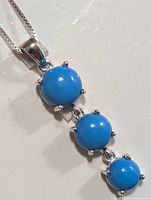 Close-up of necklace showing three round blue turquoise stones set in silver prongs, hanging vertically from silver chain.