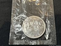 Front side of 1963 Canadian silver dollar coin in sealed packaging showing the Voyageur design.