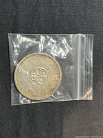 Reverse side of 1964 Canadian silver dollar showing floral design and commemorative text for 100th anniversary of Charlottetown Conference, package in clear plastic zip bag.