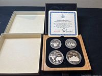 Open wooden box with lid removed showing four proof coins in capsules next to empty white tray