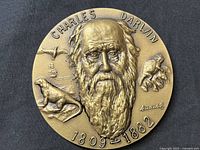 Front side of bronze medallion with high-relief portrait of Charles Darwin, surrounding elements including bird, ship, dinosaur, turtle, and inscriptions.