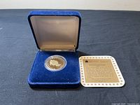 Proof coin encased in capsule, inside blue velvet case, certificate card beside it