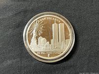 Front side of the silver commemorative medal showing Statue of Liberty, Twin Towers and NYC skyline. Inscribed with 'COOK ISLANDS' and 'WE WILL NEVER FORGET'. Medal in protective capsule on black background.