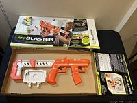 AppBlaster blaster toy laid inside the original box showing the orange and white plastic gun parts and mounting attachments.