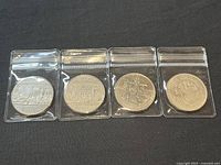 Four Canadian commemorative silver dollar coins displayed in protective plastic sleeves, showing reverse designs and condition.
