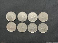 Photo showing all 8 Canadian 25-cent RCMP Centennial coins together on black fabric, displaying fronts with mounted police design.