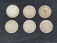 Six Canadian 25 cents silver coins arranged in two rows of three on black fabric background, showing country and denomination markings.