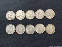 Ten Canadian 25 cents silver coins arranged in two rows on black fabric background showing reverse side with caribou design.