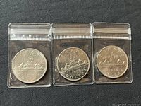 Three 1969 Canadian silver dollar coins, each in a transparent protective plastic sleeve, laid out on a black surface showing the reverse side with the Voyageur canoe design.