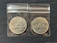 Two 1972 Canada silver dollar coins in protective plastic sleeves showing reverse side with Voyageur design and date 1972
