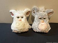 Front view of both Furbys side by side on black surface against wall
